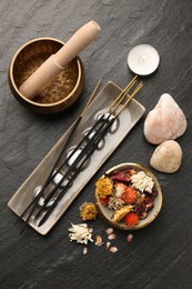 Photo of Incense sticks, Tibetan singing bowl, stones, dry flowers and candle on black table, flat lay