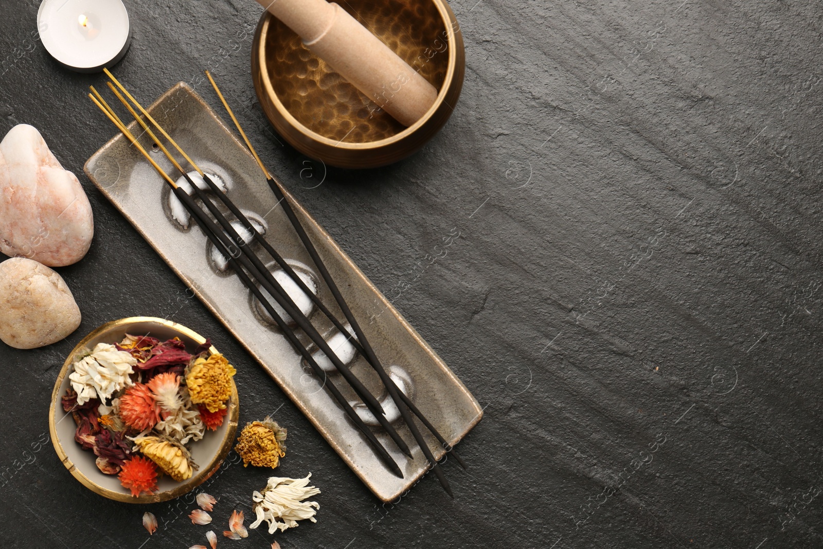 Photo of Incense sticks, Tibetan singing bowl, stones, dry flowers and candle on black table, flat lay. Space for text