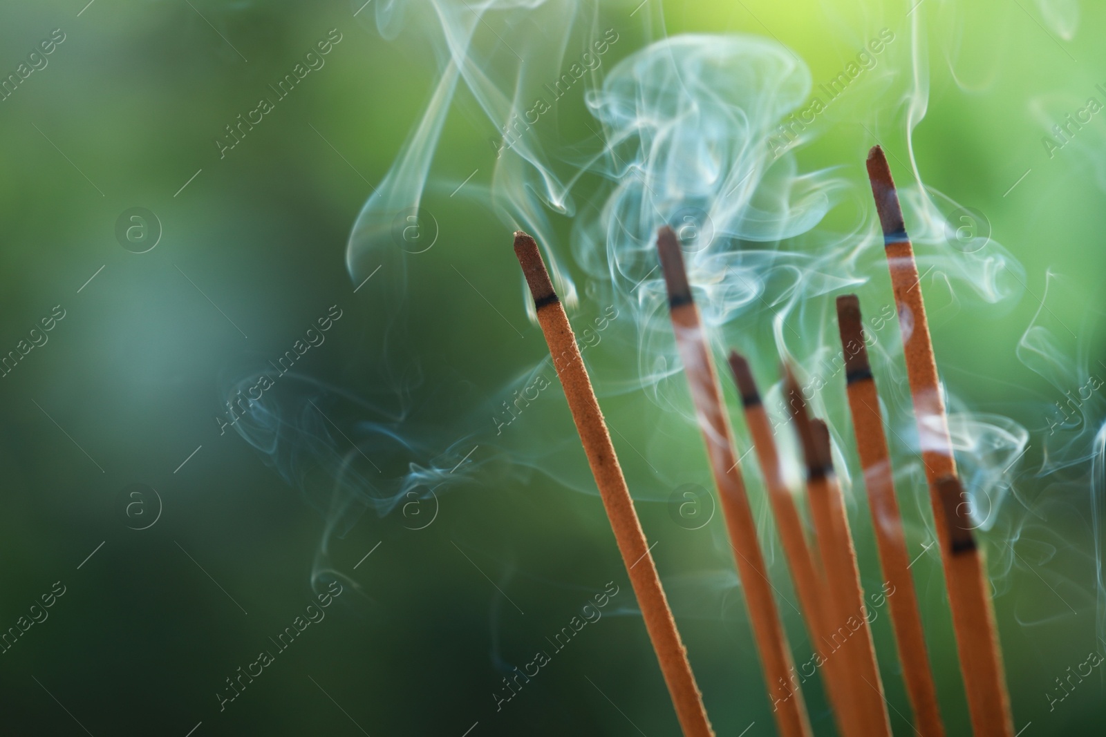 Photo of Incense sticks smoldering on green blurred background, space for text