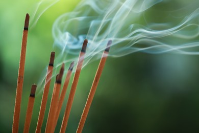 Photo of Incense sticks smoldering on green blurred background, space for text