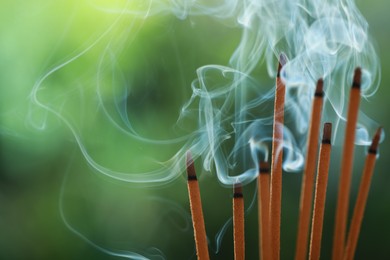 Photo of Incense sticks smoldering on green blurred background, space for text