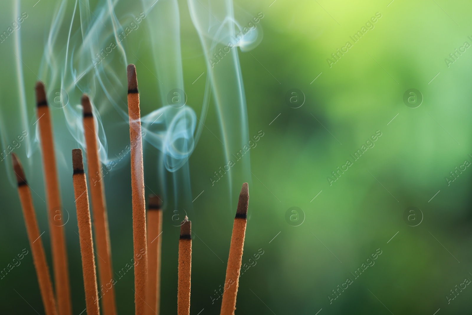 Photo of Incense sticks smoldering on green blurred background, space for text