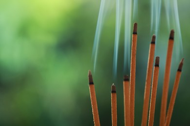 Photo of Incense sticks smoldering on green blurred background, space for text