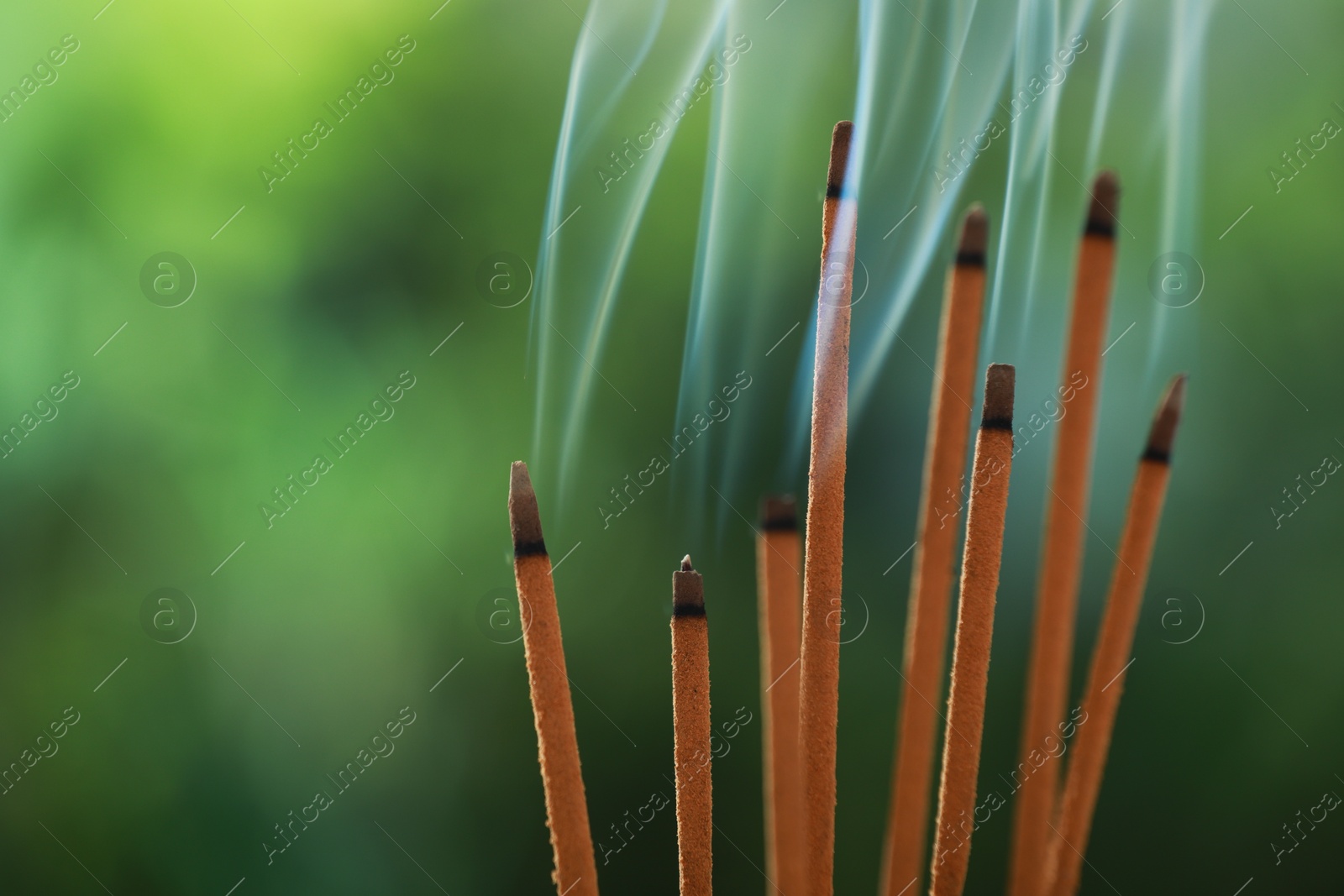 Photo of Incense sticks smoldering on green blurred background, space for text