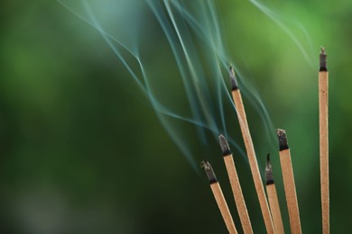 Incense sticks smoldering on green blurred background, space for text