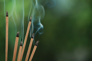 Incense sticks smoldering on green blurred background, space for text