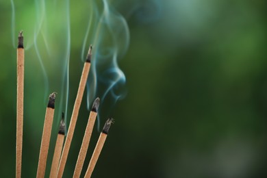 Photo of Incense sticks smoldering on green blurred background, space for text