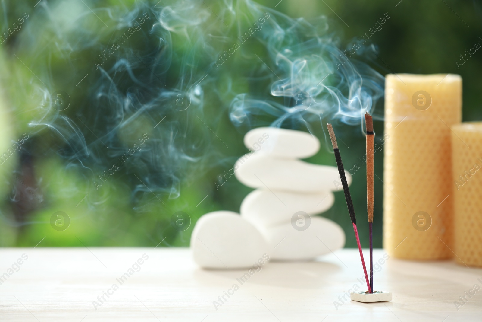 Photo of Incense sticks smoldering near stones and candles on wooden table outdoors, space for text