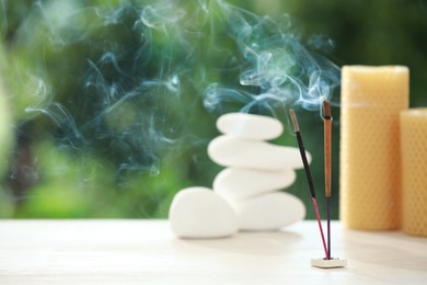 Incense sticks smoldering near stones and candles on wooden table outdoors, space for text