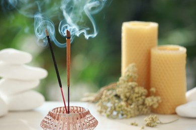 Incense sticks smoldering in holder near stones, candles and dry flowers on table outdoors