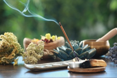 Incense stick smoldering in holder, candles and dry flowers on wooden table outdoors