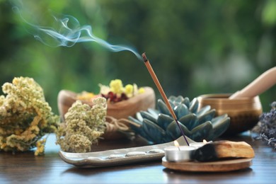 Incense stick smoldering in holder, candles and dry flowers on wooden table outdoors
