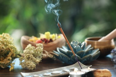 Incense stick smoldering in holder, candles and dry flowers on wooden table outdoors