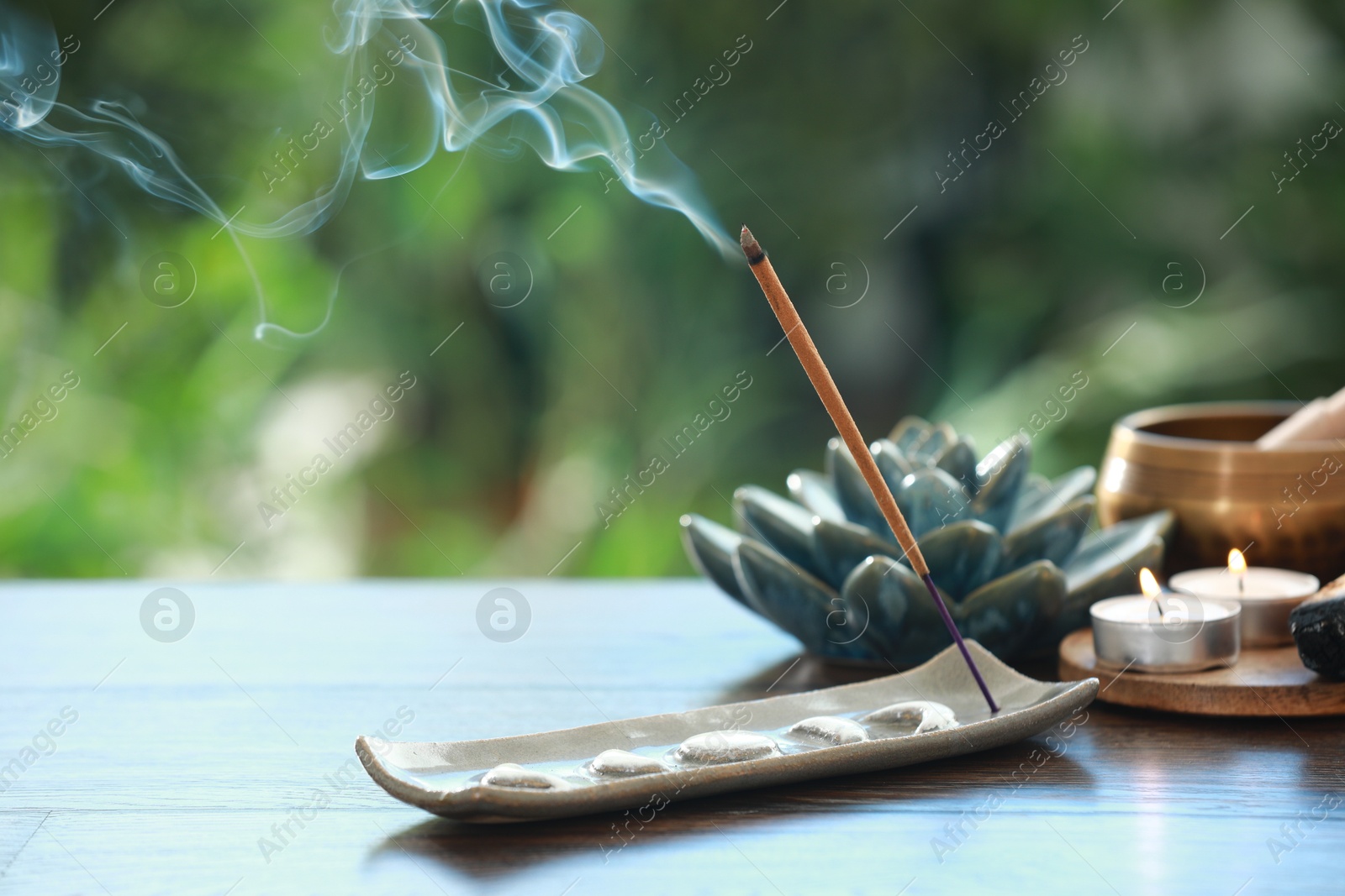 Photo of Incense stick smoldering in holder and burning candles on wooden table outdoors