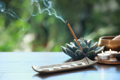 Incense stick smoldering in holder and burning candles on wooden table outdoors