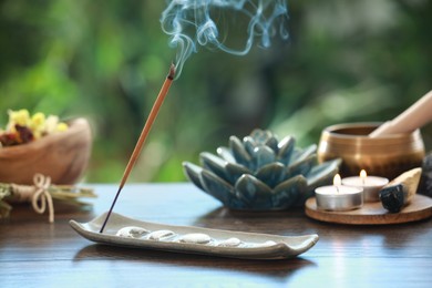 Photo of Incense stick smoldering in holder and burning candles on wooden table outdoors