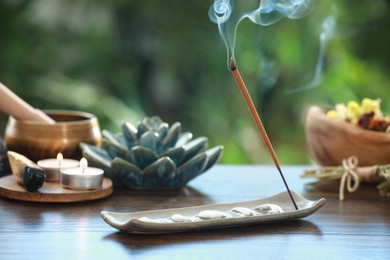 Incense stick smoldering in holder and burning candles on wooden table outdoors