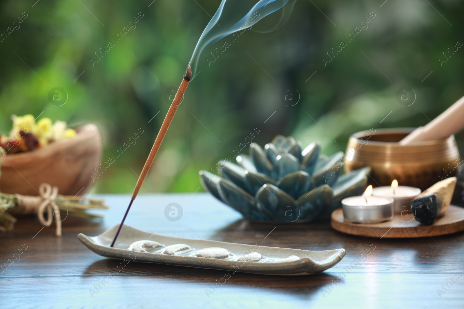 Photo of Incense stick smoldering in holder and burning candles on wooden table outdoors