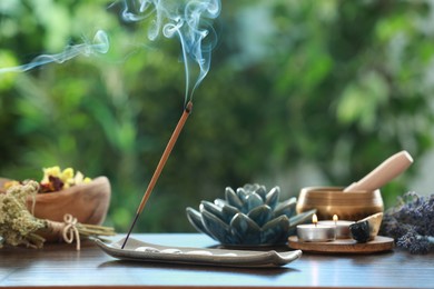Incense stick smoldering in holder, burning candles, dry flowers and Tibetan singing bowl on wooden table outdoors