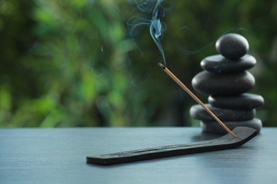 Incense stick smoldering in holder and spa stones on wooden table outdoors, space for text. Om ligature