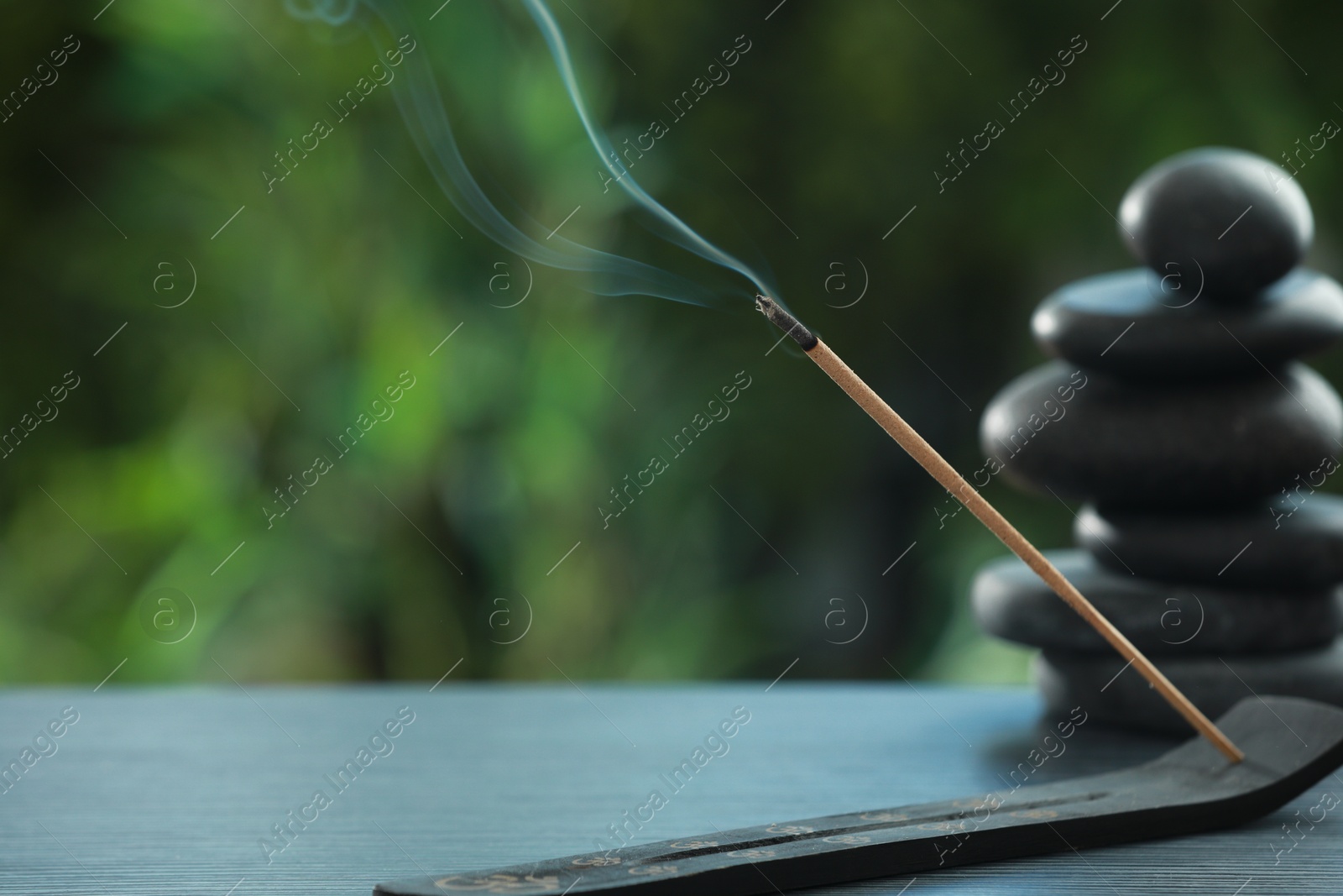 Photo of Incense stick smoldering in holder and spa stones on wooden table outdoors, space for text. Om ligature