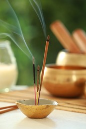 Incense sticks smoldering in holder, Tibetan singing bowl and candle on light table outdoors