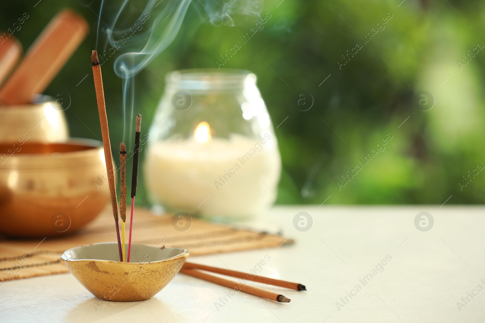 Photo of Incense sticks smoldering in holder, Tibetan singing bowl and candle on light table outdoors, space for text