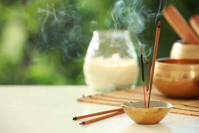 Incense sticks smoldering in holder, Tibetan singing bowl and candle on light table outdoors, space for text