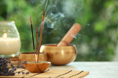 Incense sticks smoldering in holder, Tibetan singing bowls, dried lavender and candle on light table outdoors