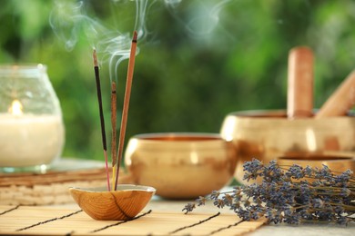 Incense sticks smoldering in holder, Tibetan singing bowls, dried lavender and candle on table outdoors