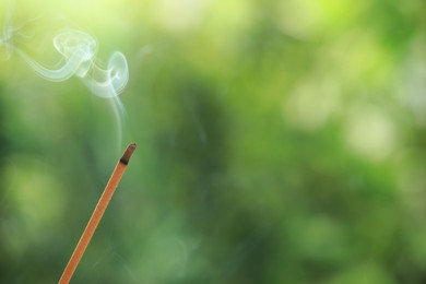 Incense stick smoldering on green blurred background, space for text