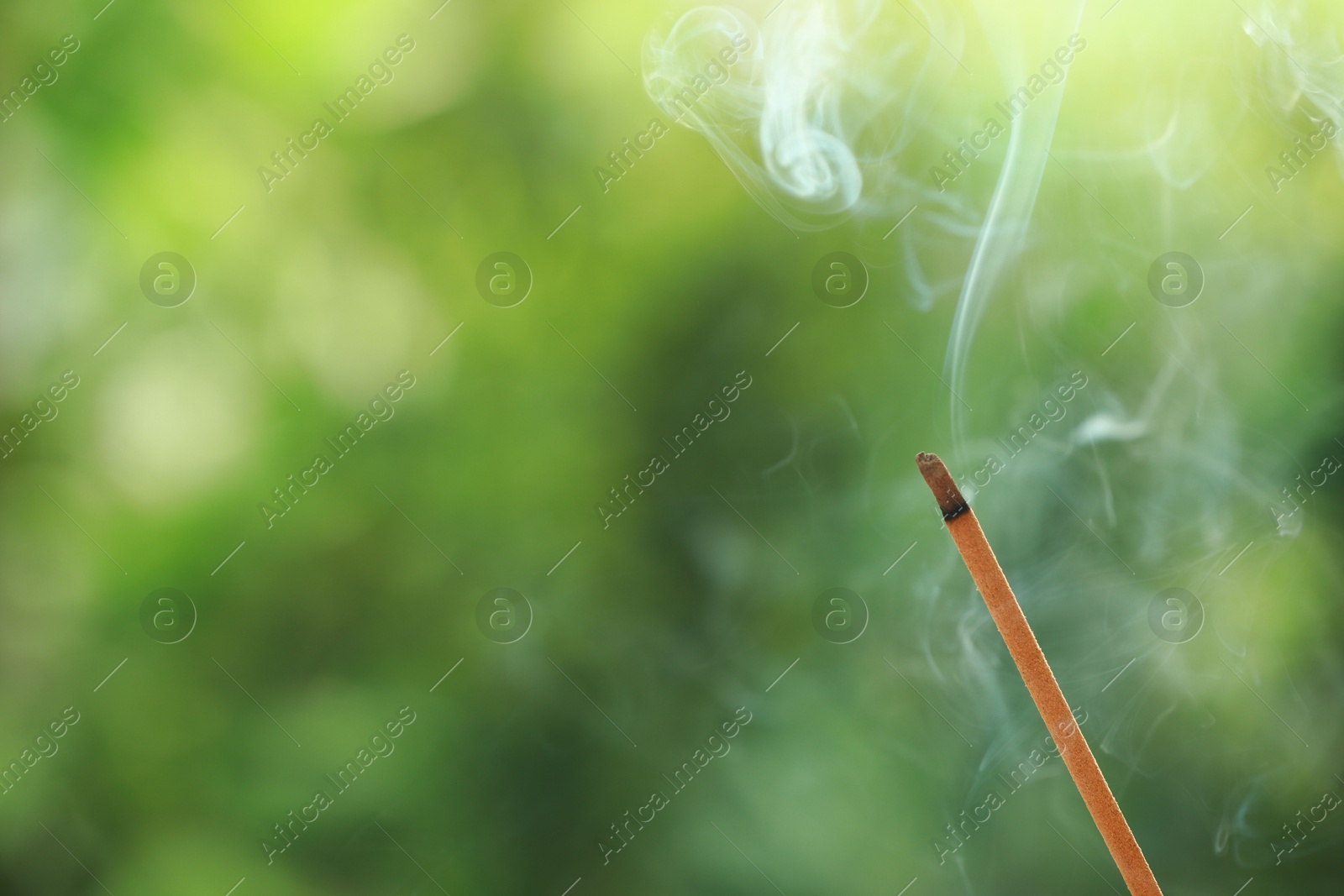 Photo of Incense stick smoldering on green blurred background, space for text