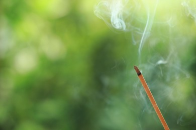 Incense stick smoldering on green blurred background, space for text