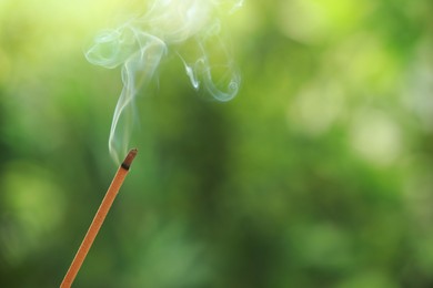 Photo of Incense stick smoldering on green blurred background, space for text