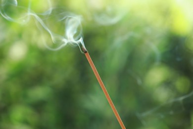 Photo of Incense stick smoldering on green blurred background