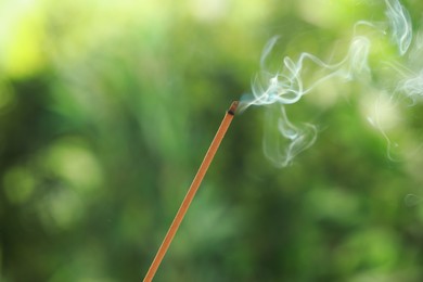 Incense stick smoldering on green blurred background