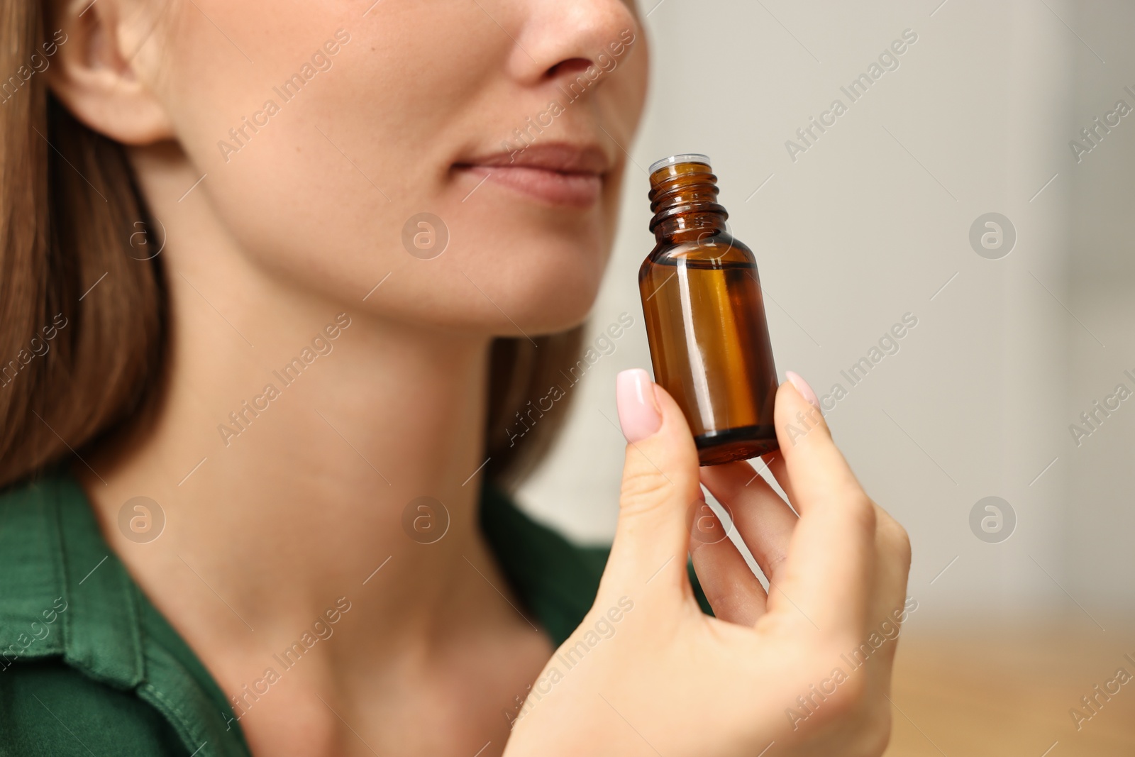 Photo of Aromatherapy. Woman with bottle of essential oil on light background, closeup