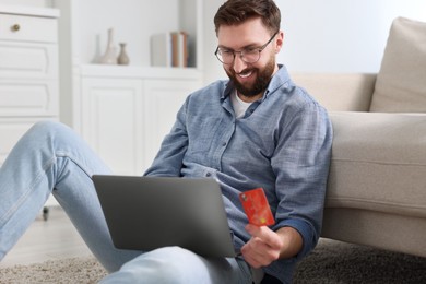 Photo of Online banking. Happy young man with credit card and laptop paying purchase at home