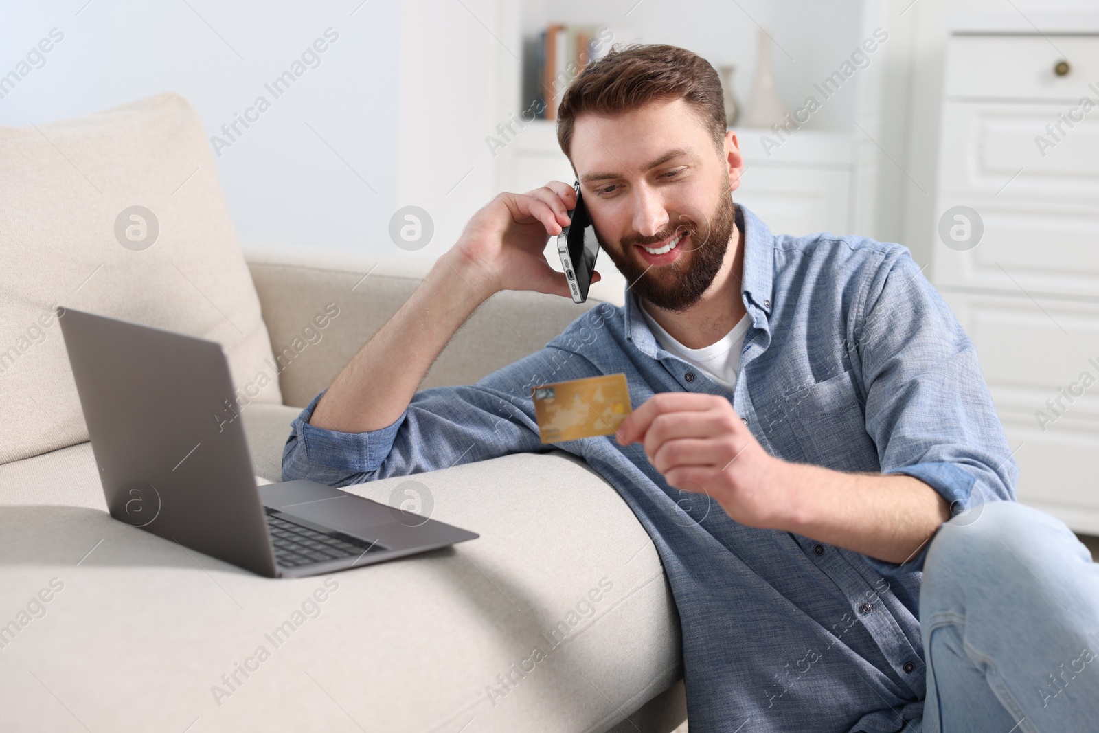 Photo of Online banking. Happy young man with credit card talking by smartphone at home