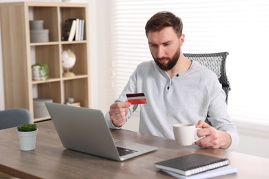 Online banking. Young man with credit card and laptop paying purchase at table indoors