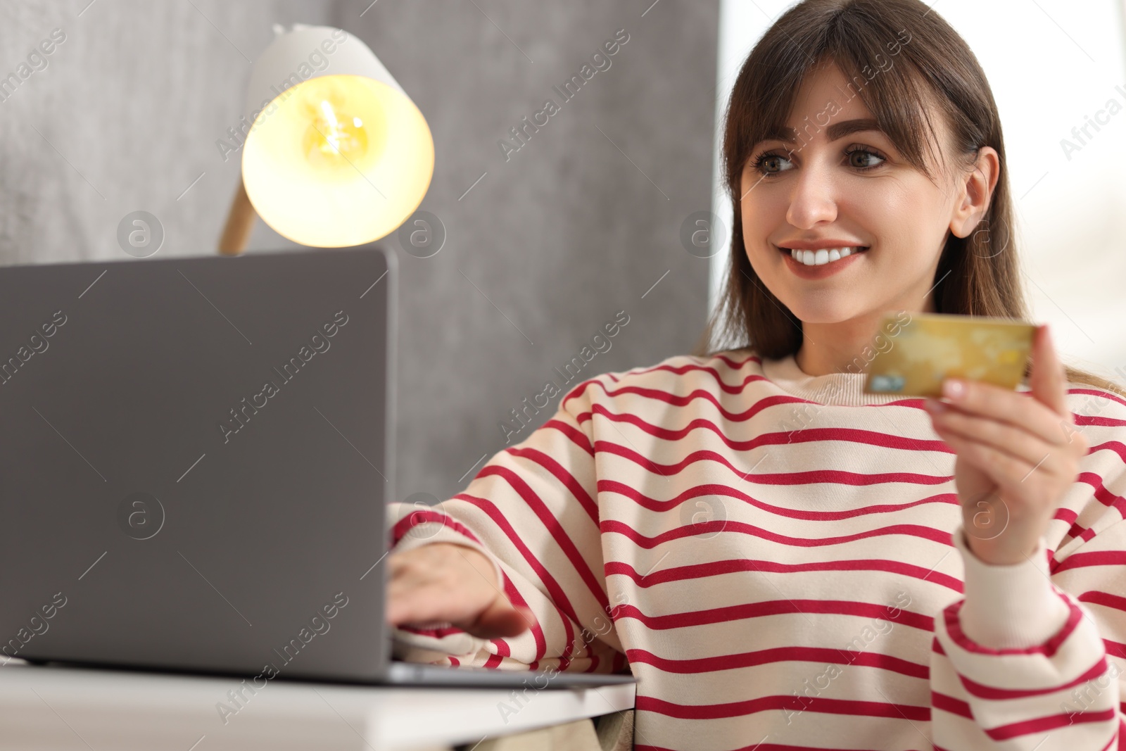 Photo of Online banking. Smiling woman with credit card and laptop paying purchase at table indoors