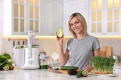 Smiling woman with juicer and fresh products at white marble table in kitchen