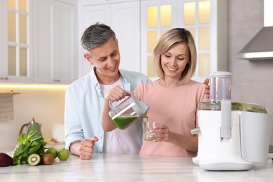 Happy couple with juicer, fresh products and tasty juice at white marble table in kitchen