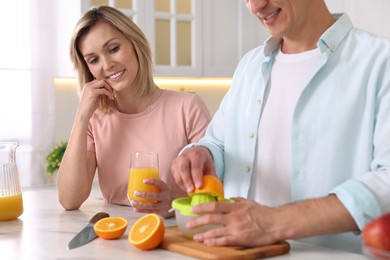 Happy couple with juicer and fresh products making juice at white marble table in kitchen, closeup