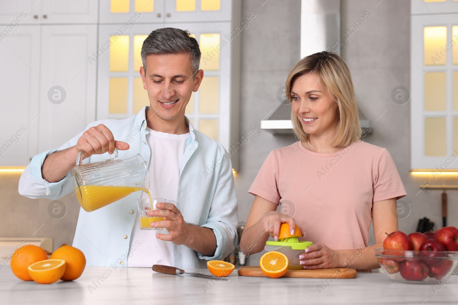 Photo of Happy couple with juicer and fresh products making juice at white marble table in kitchen