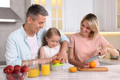 Photo of Happy family making juice at white marble table in kitchen