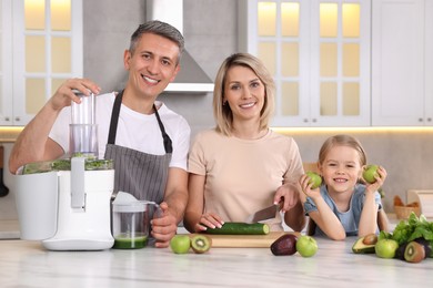 Happy family with juicer and fresh products making drink at white marble table in kitchen