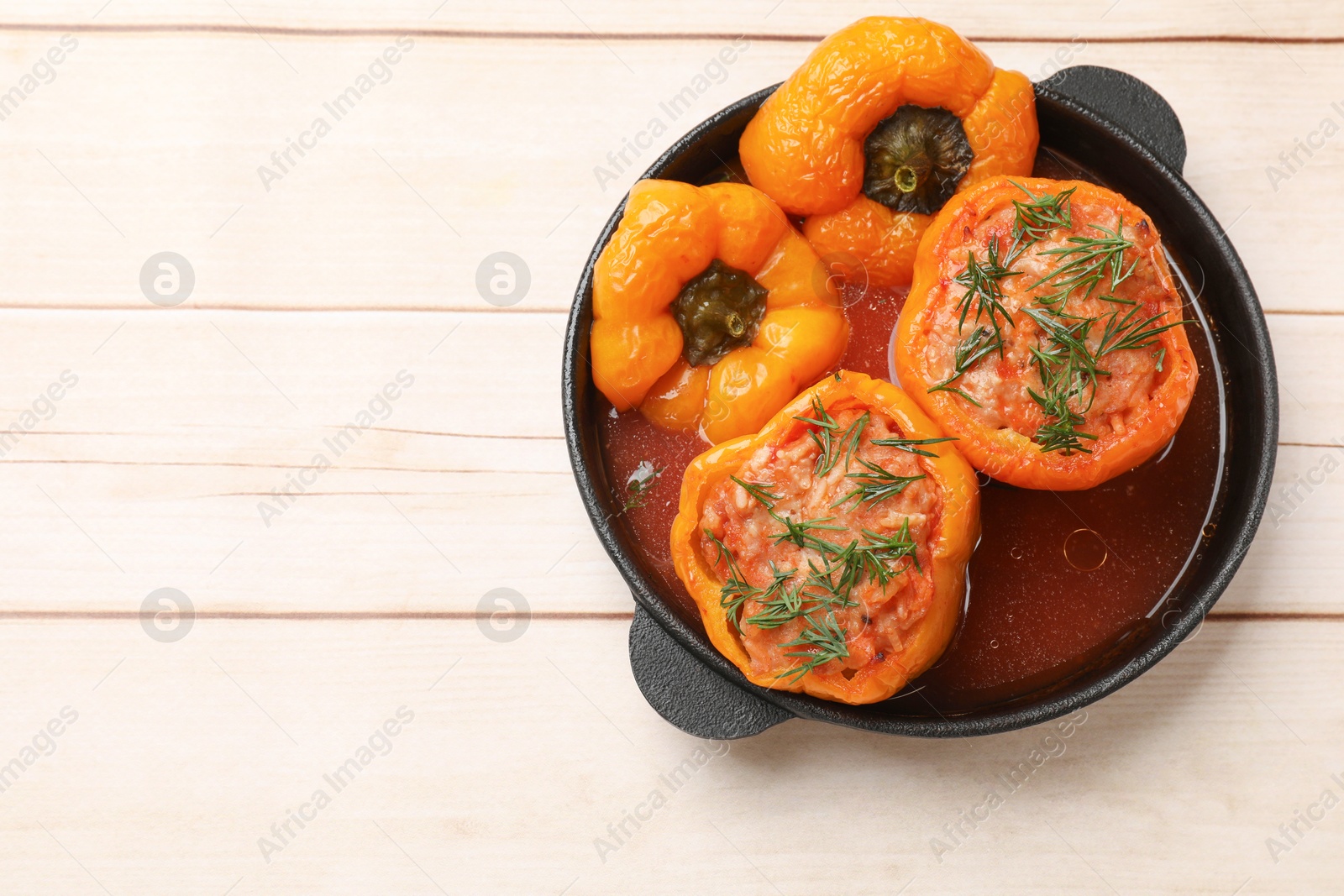 Photo of Tasty stuffed peppers in pan on light wooden table, top view. Space for text