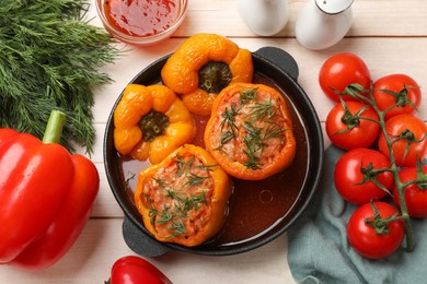 Photo of Tasty stuffed peppers in pan, sauce and products on light wooden table, flat lay