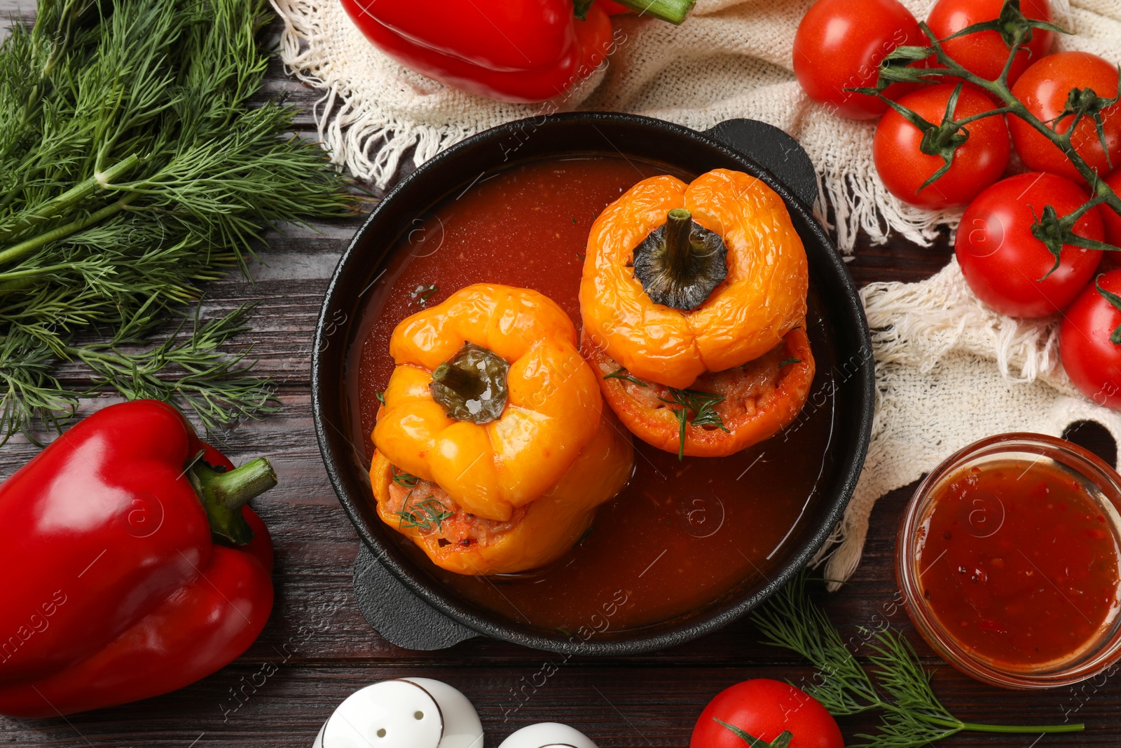 Photo of Tasty stuffed peppers in pan, sauce and products on wooden table, flat lay